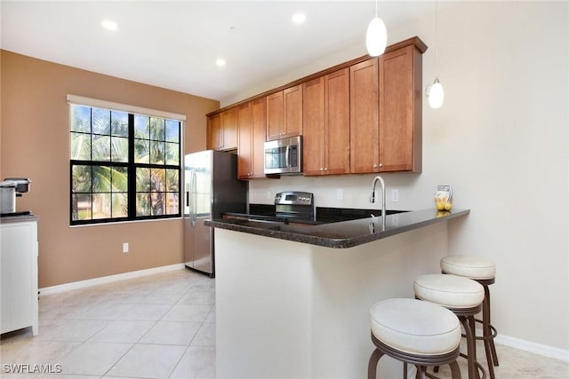 kitchen featuring hanging light fixtures, kitchen peninsula, dark stone counters, a breakfast bar area, and appliances with stainless steel finishes