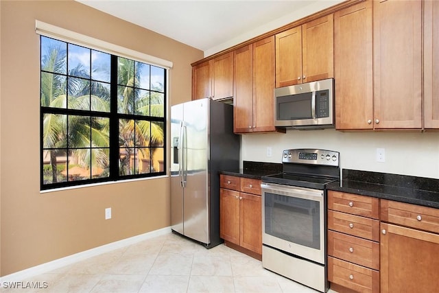 kitchen featuring light tile patterned floors, stainless steel appliances, and dark stone counters