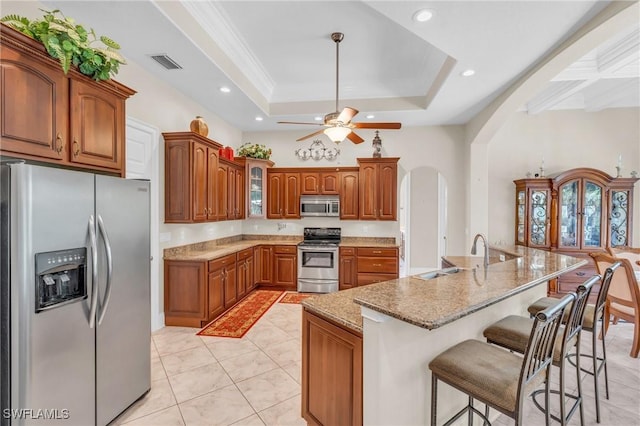 kitchen featuring ceiling fan, sink, stainless steel appliances, a raised ceiling, and a kitchen island with sink