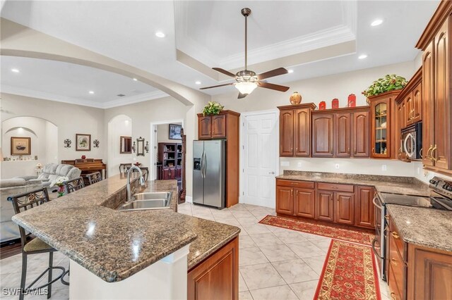 kitchen with a kitchen breakfast bar, stainless steel appliances, a raised ceiling, and a kitchen island with sink