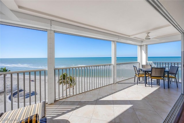 sunroom featuring ceiling fan, a water view, and a beach view