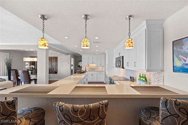 kitchen with pendant lighting, stove, white cabinets, decorative backsplash, and a breakfast bar area