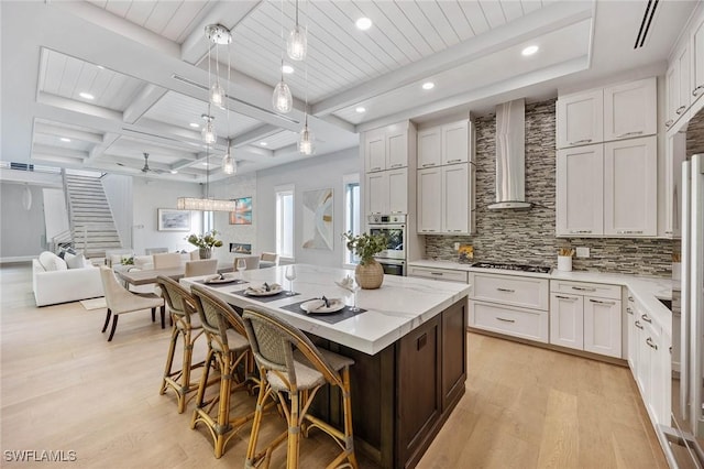 kitchen with gas cooktop, a kitchen island, backsplash, wall chimney exhaust hood, and light wood finished floors