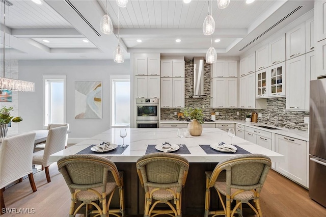 kitchen with stainless steel appliances, a sink, decorative backsplash, and wall chimney exhaust hood