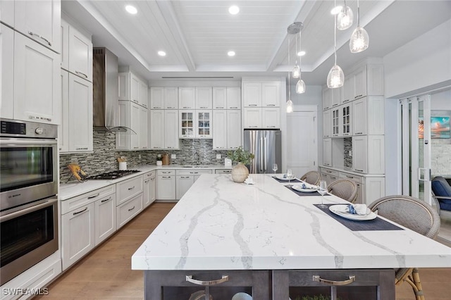 kitchen featuring a breakfast bar area, a spacious island, appliances with stainless steel finishes, wall chimney range hood, and glass insert cabinets