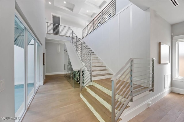 stairway with baseboards, coffered ceiling, wood finished floors, a high ceiling, and beam ceiling