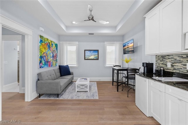 living area featuring visible vents, baseboards, ceiling fan, a tray ceiling, and light wood-style floors