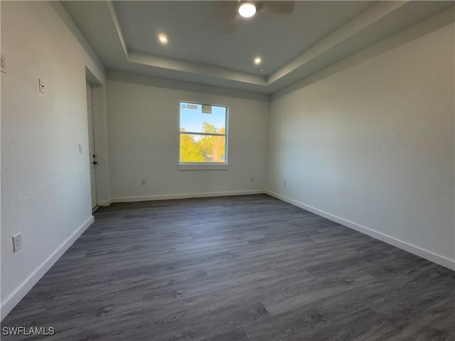 empty room with ceiling fan, dark hardwood / wood-style floors, and a tray ceiling