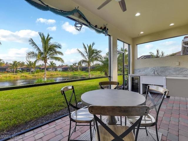 sunroom featuring wine cooler, ceiling fan, sink, and a water view