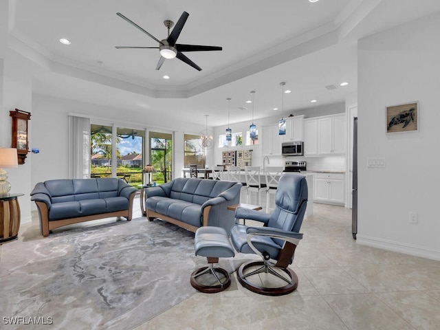 living room with a raised ceiling, ceiling fan, and ornamental molding