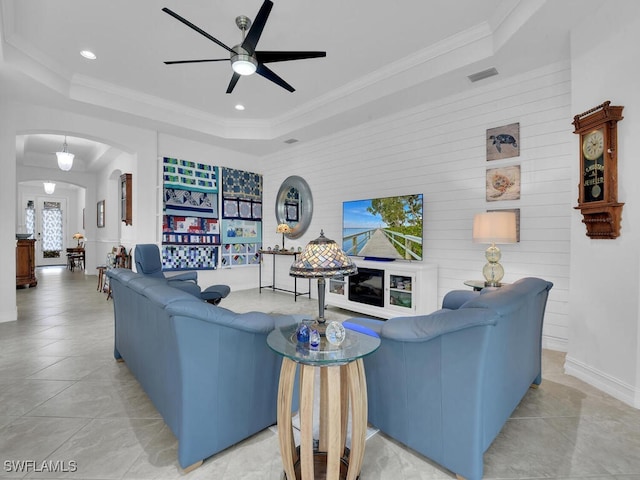 tiled living room with ceiling fan, a raised ceiling, and ornamental molding