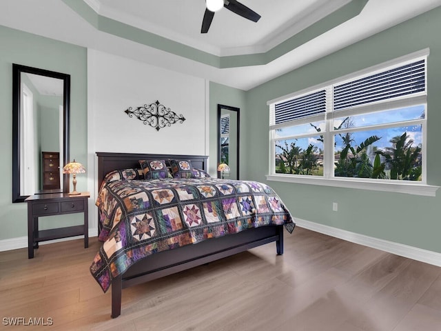 bedroom featuring a raised ceiling, ceiling fan, crown molding, and hardwood / wood-style flooring