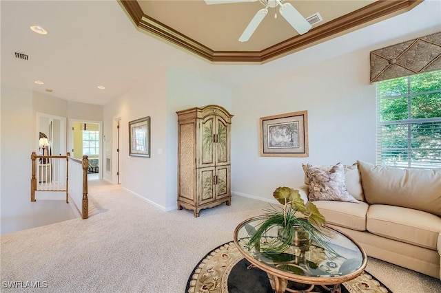 living room featuring a tray ceiling, crown molding, ceiling fan, and light colored carpet