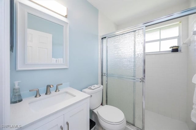 bathroom featuring a shower with door, vanity, and toilet