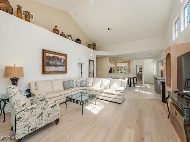 living room with light hardwood / wood-style flooring, a towering ceiling, and ceiling fan with notable chandelier