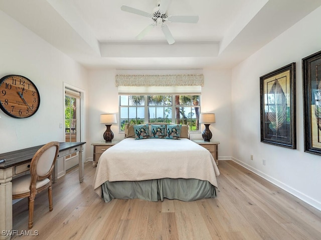 bedroom with ceiling fan, light hardwood / wood-style flooring, and a tray ceiling