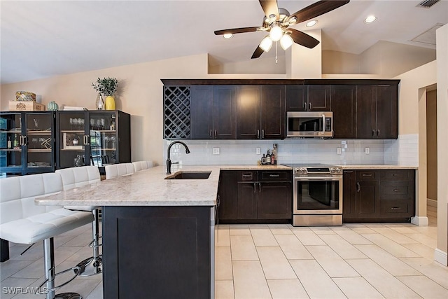 kitchen with lofted ceiling, sink, decorative backsplash, appliances with stainless steel finishes, and a breakfast bar area