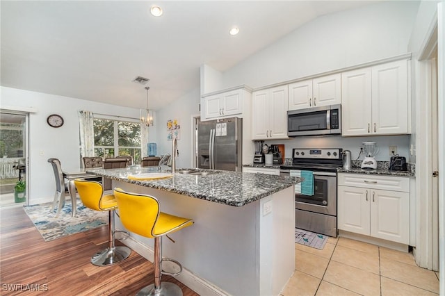 kitchen with appliances with stainless steel finishes, a center island with sink, white cabinetry, hanging light fixtures, and lofted ceiling