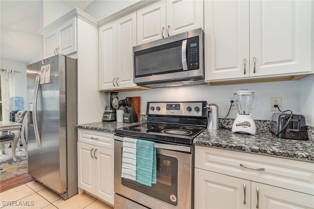 kitchen with appliances with stainless steel finishes, light tile patterned floors, white cabinetry, and dark stone counters