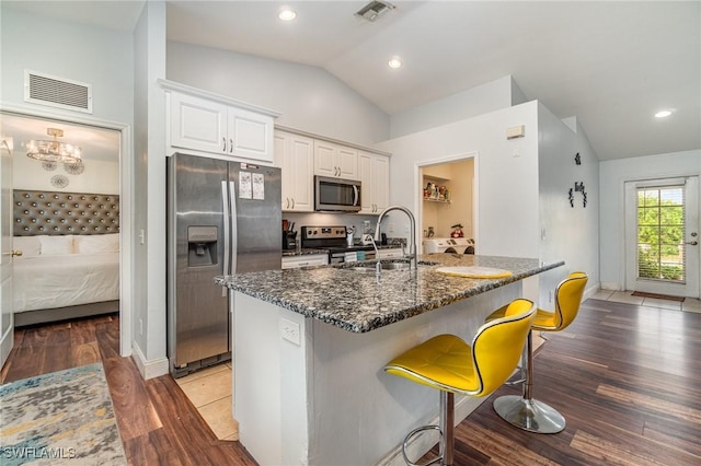 kitchen with appliances with stainless steel finishes, dark stone counters, sink, white cabinets, and lofted ceiling