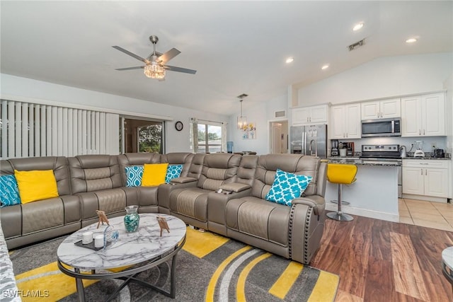 living room with ceiling fan with notable chandelier, light hardwood / wood-style flooring, and vaulted ceiling