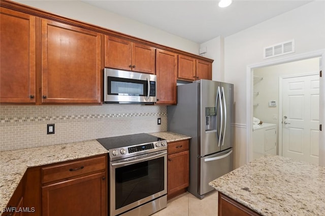 kitchen with tasteful backsplash, washing machine and dryer, light stone counters, and stainless steel appliances