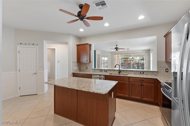 kitchen with kitchen peninsula, appliances with stainless steel finishes, light stone countertops, sink, and a center island