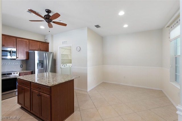 kitchen with ceiling fan, light stone counters, a kitchen island, washer and dryer, and appliances with stainless steel finishes