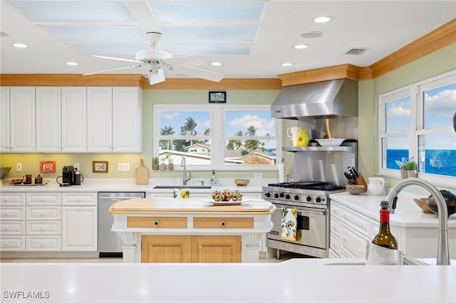 kitchen with ceiling fan, sink, stainless steel appliances, wall chimney range hood, and white cabinets