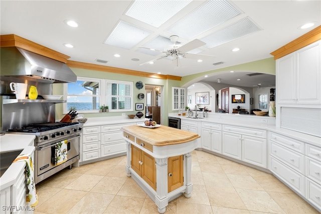 kitchen featuring kitchen peninsula, high end stove, extractor fan, a center island, and white cabinetry