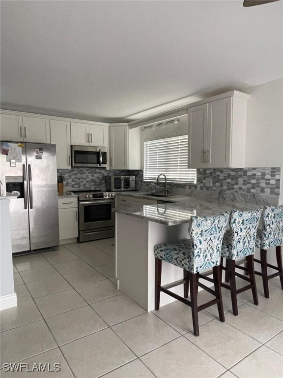 kitchen with sink, stainless steel appliances, kitchen peninsula, a breakfast bar area, and light tile patterned floors