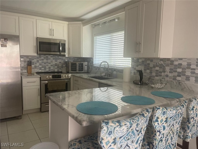 kitchen with light stone countertops, appliances with stainless steel finishes, sink, white cabinets, and light tile patterned flooring