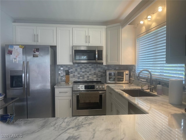 kitchen with backsplash, sink, appliances with stainless steel finishes, light stone counters, and white cabinetry