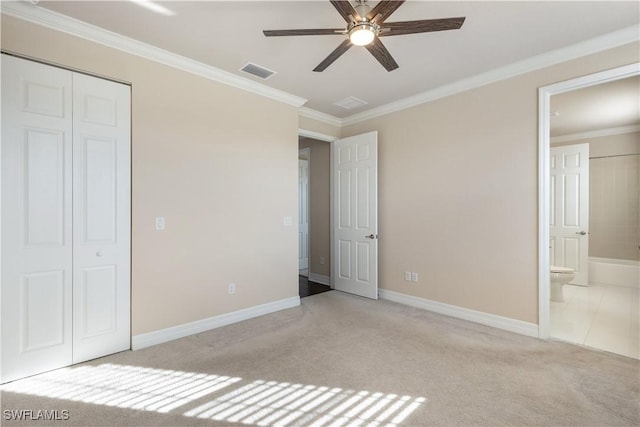 unfurnished bedroom featuring light carpet, ensuite bath, ceiling fan, crown molding, and a closet