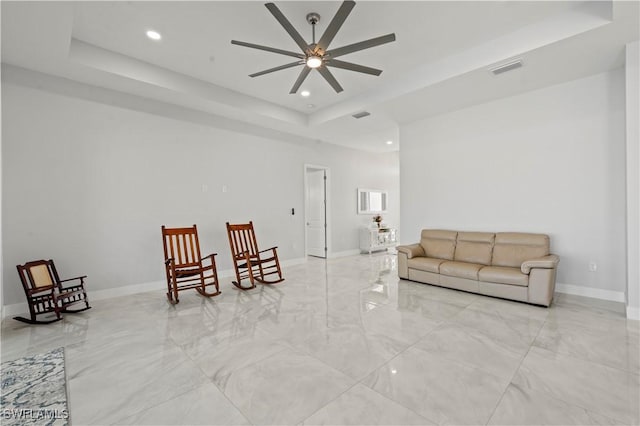 living area featuring ceiling fan and a tray ceiling