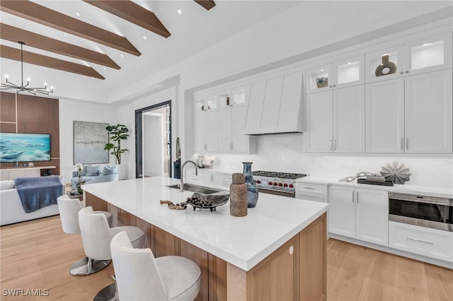 kitchen with decorative backsplash, a kitchen island with sink, sink, and white cabinets