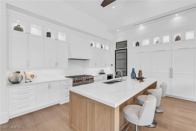 kitchen with tasteful backsplash, sink, a center island with sink, range with two ovens, and white cabinetry