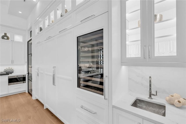 kitchen featuring white cabinetry, sink, beverage cooler, backsplash, and light hardwood / wood-style floors