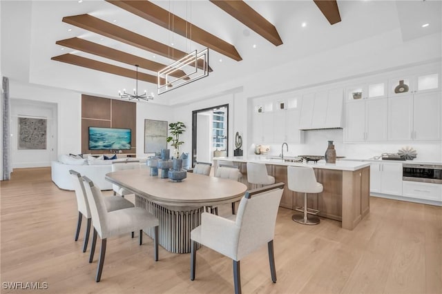 dining space featuring an inviting chandelier, sink, light wood-type flooring, a towering ceiling, and beamed ceiling