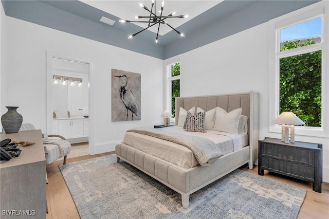 bedroom with a notable chandelier, light hardwood / wood-style floors, and ensuite bath