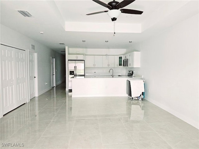 kitchen with stainless steel appliances, a raised ceiling, ceiling fan, sink, and white cabinetry