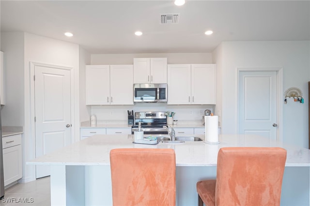 kitchen featuring white cabinetry, sink, light stone countertops, stainless steel appliances, and a kitchen island with sink