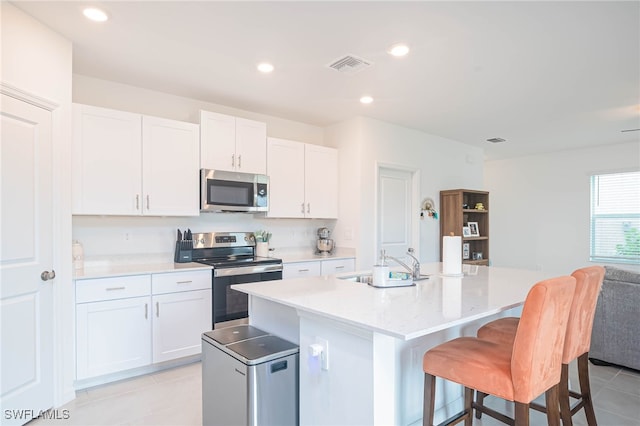 kitchen featuring white cabinets, appliances with stainless steel finishes, sink, and an island with sink