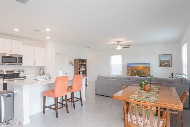 kitchen featuring appliances with stainless steel finishes, a kitchen breakfast bar, ceiling fan, white cabinets, and light tile patterned flooring