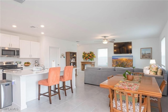 kitchen featuring white cabinetry, ceiling fan, stainless steel appliances, a fireplace, and a center island with sink