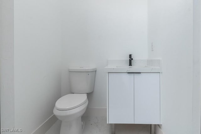 bathroom with toilet, marble finish floor, baseboards, and vanity