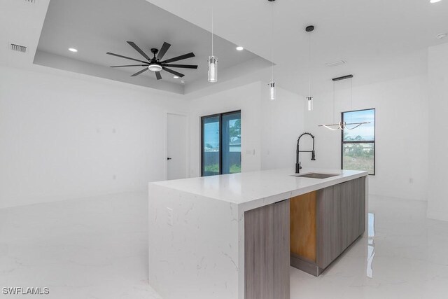 kitchen with marble finish floor, brown cabinets, a raised ceiling, a sink, and modern cabinets