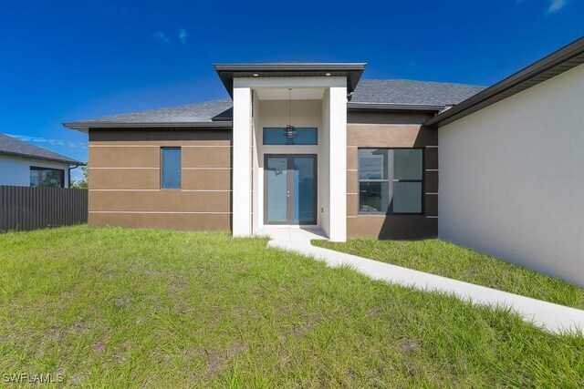 back of property with a shingled roof, fence, a yard, french doors, and stucco siding