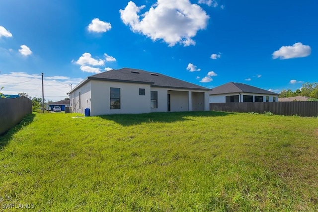 rear view of property featuring a lawn, fence, and stucco siding