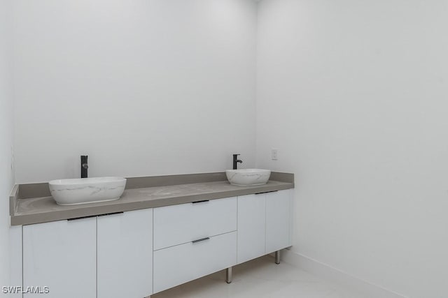 bathroom with double vanity, marble finish floor, baseboards, and a sink